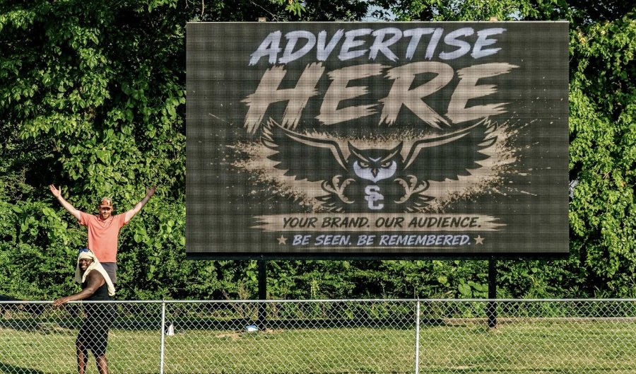 17ft by 10ft outdoor LED videoboard beside a ball field running an "Advertise Here" sponsorship graphic with an owl mascot